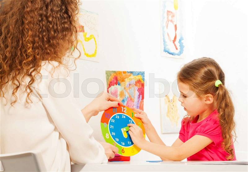 Schoolgirl moving pointers at the dial of colored clock model in the classroom, stock photo