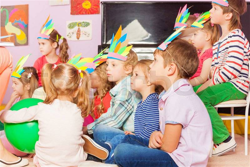 Many kids boys and girls sit in developmental kindergarten class together wearing handmade headwear, stock photo