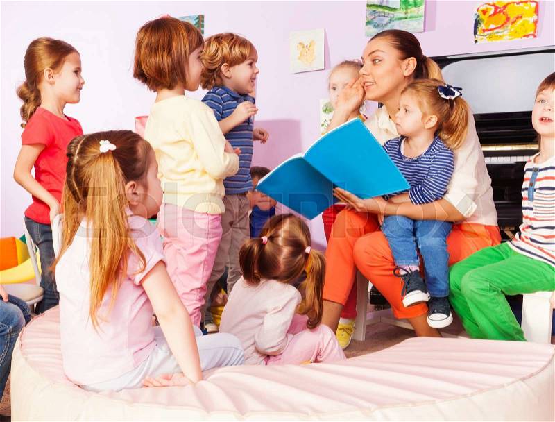 Teacher with kids boys and girls read and discuss book sitting together in the class, stock photo