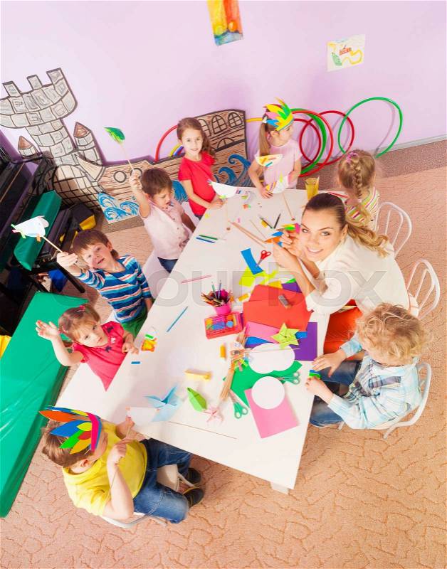 Group of kids boys and girls sit around the table in kindergarten with teacher view from above , stock photo