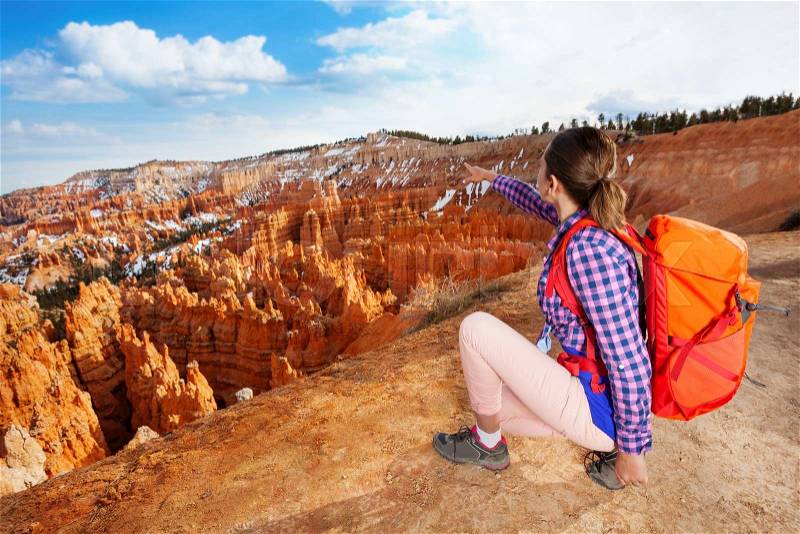 Young woman point to Bryce canyon sitting on the edge of the cliff pointing to the rocks, stock photo