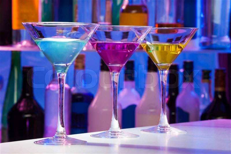 Three cocktail glasses standing on the bar table with different colors drinks, stock photo