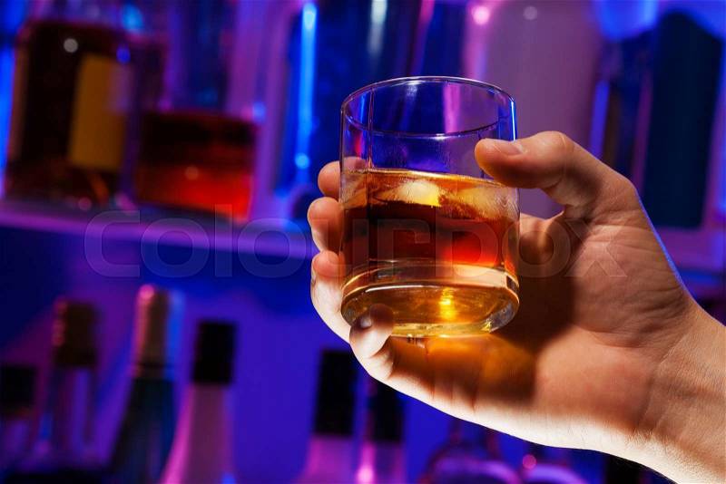 Close-up of Man hand holding whiskey in the glass with bar background and shelves with bottles on back , stock photo