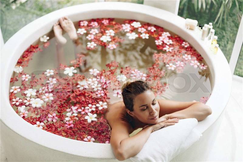 Woman relaxing in round outdoor bath with tropical flowers, organic skin care, luxury spa hotel, lifestyle photo, top view, stock photo