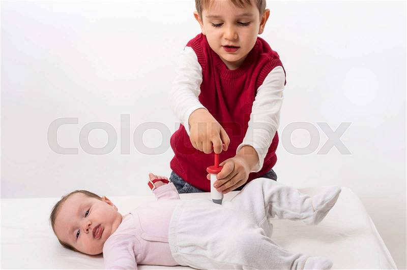 Brother paying as doctor and patient with his baby sister. The boy makes injection with syringe, stock photo