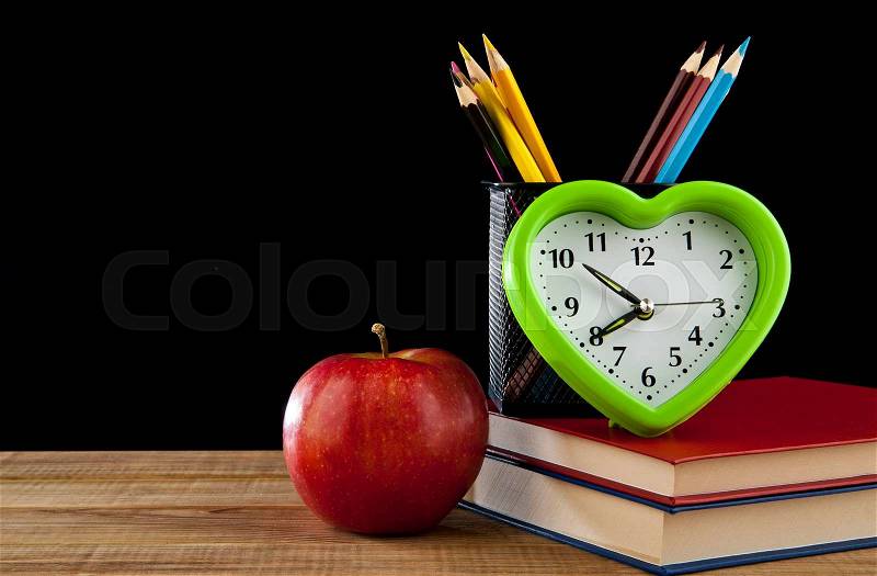 Apple, pencils, books and clock on black background, stock photo