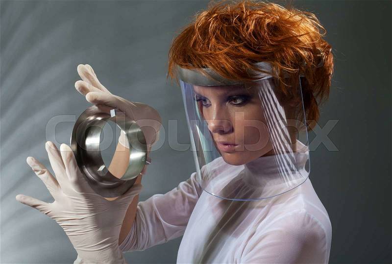 Futuristic woman examine metal detail holding it in latex gloves and wearing white clothes made with professional makeup and hair stylist, stock photo