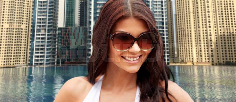 Summer vacation, tourism, travel, holidays and people concept - face of smiling young woman with sunglasses over infinity edge swimming pool in dubai city background, stock photo