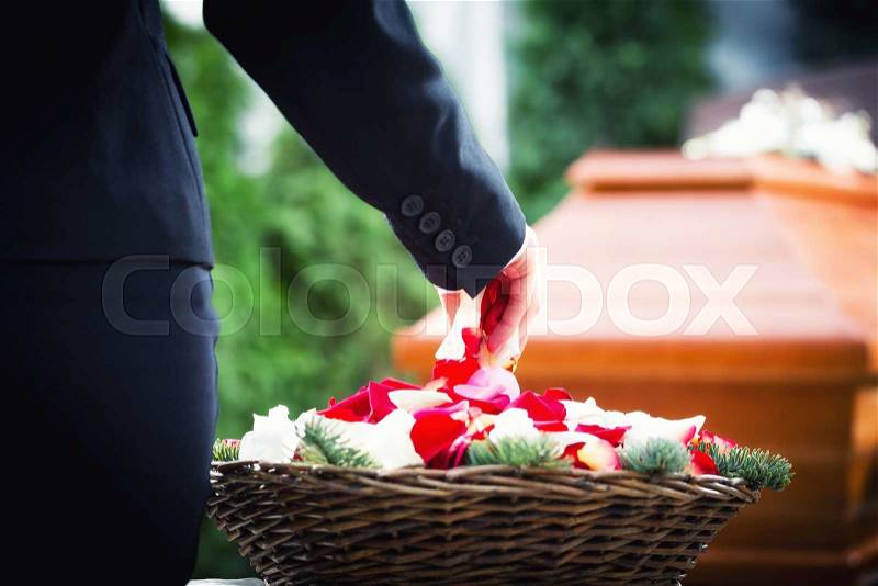 Woman on funeral putting rose petals on coffin, stock photo