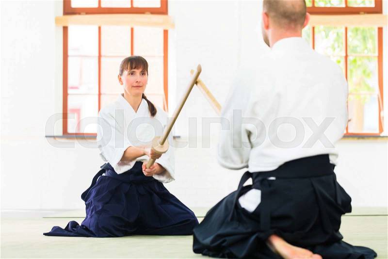 Man and woman fighting with wooden swords at Aikido training in martial arts school , stock photo