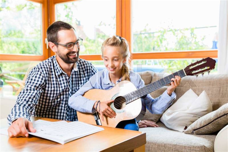 Father and daughter learning play the guitar, making music together, stock photo
