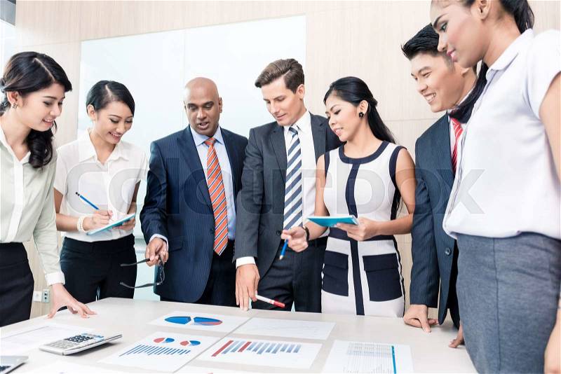 Business team discussing graphs and numbers in meeting, men and women of Chinese, Caucasian, Indonesian, and Indian ethnicity, stock photo