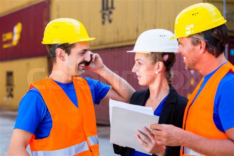 Worker and manager of shipment company discussing freight or shipment documents, one man is using phone or walkie-talkie, stock photo