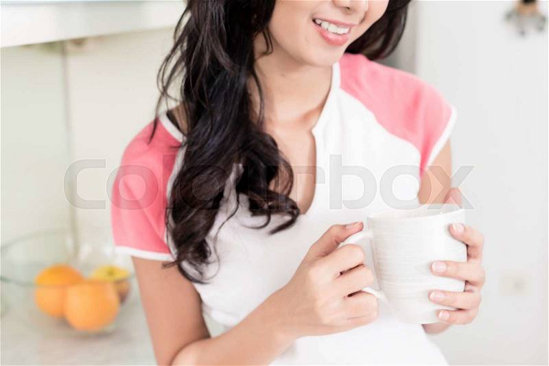 Woman drinking tea or coffee in her Asian kitchen, stock photo