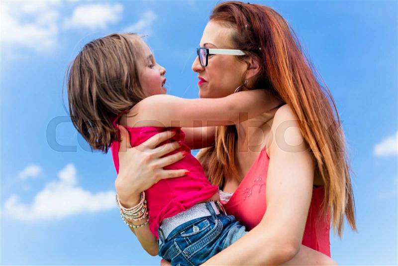Mother carrying daughter on her arm under a clear blue summer sky, stock photo
