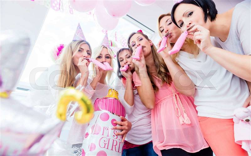 Group of women on baby shower party having fun wearing party hats blowing paper streamer, stock photo