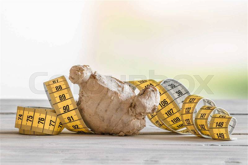 Ginger root with yellow measure tape on a table, stock photo
