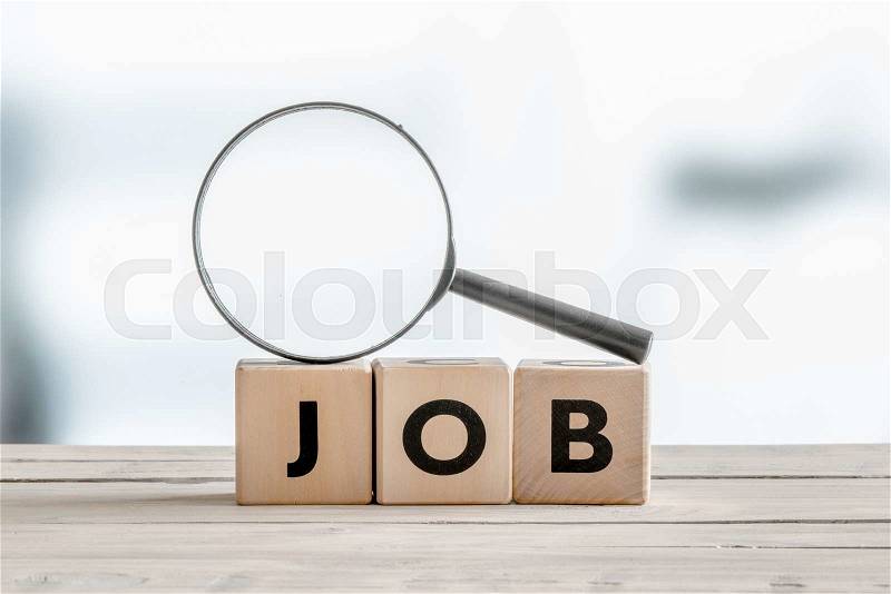 Magnifying glass on the word job on a wooden table, stock photo