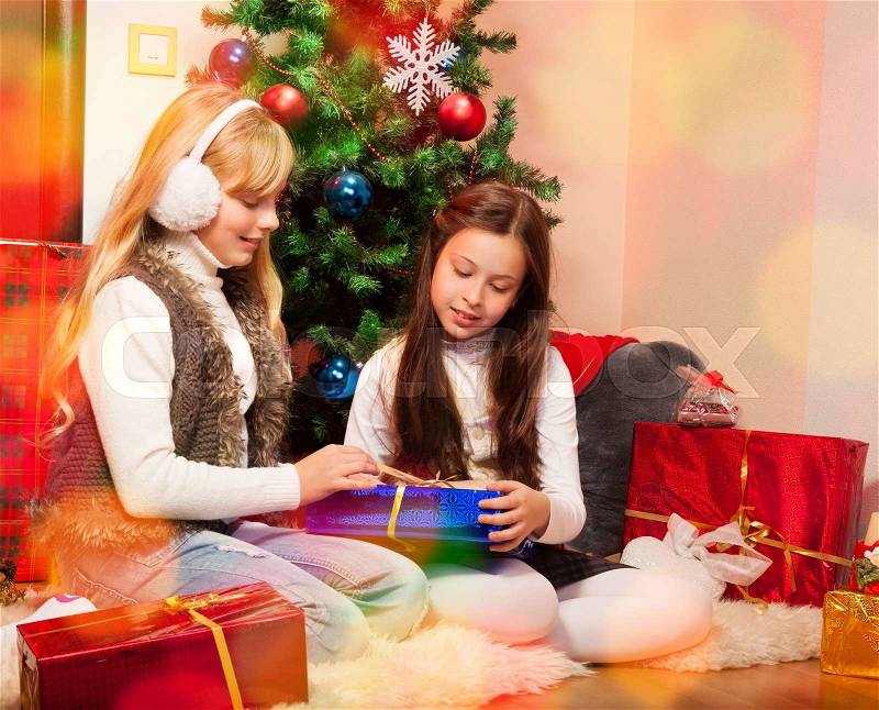 Friends giving presents each other sitting near christmas tree, stock photo
