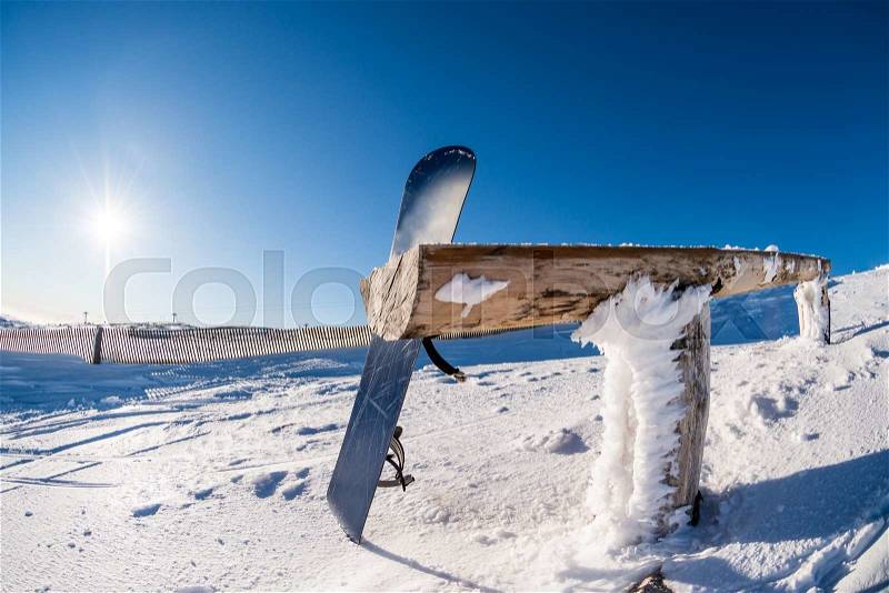 Snowboard leaning on a wood rail on a winter snow covered mountainside and sun shine in blue sky, stock photo