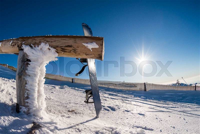 Snowboard leaning on a wood rail on a winter snow covered mountainside and sun shine in blue sky, stock photo