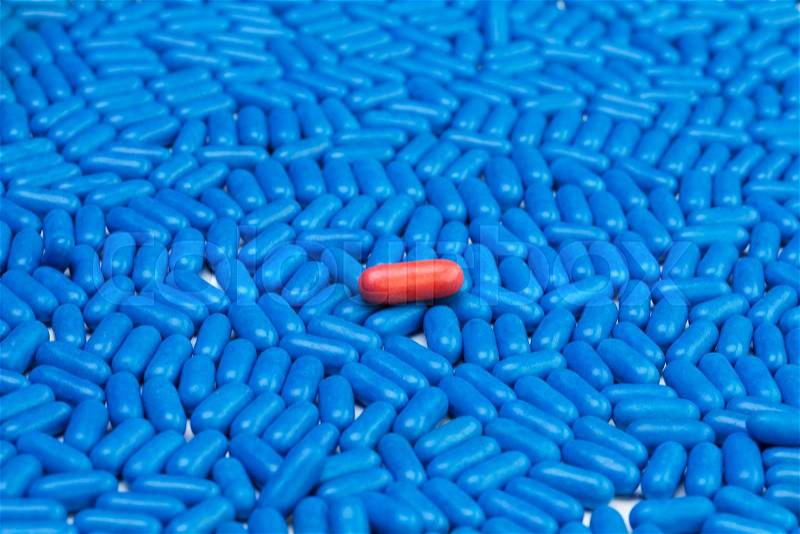 One red drug pill laying on many blue tablets, stock photo