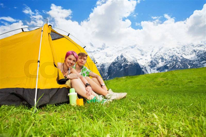 Happy young couple sitting in the yellow tent on the mountain plateau field, stock photo