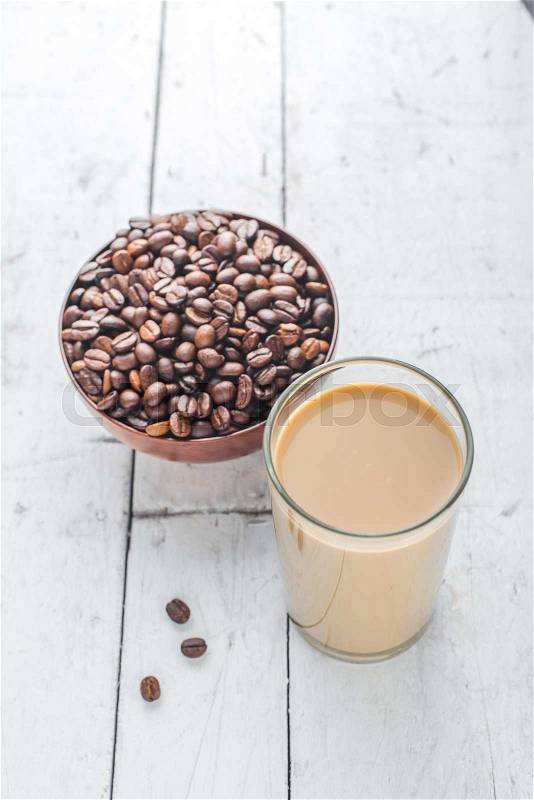 Coffee beans in bowl and a glass of coffee milk on wooden table, stock photo