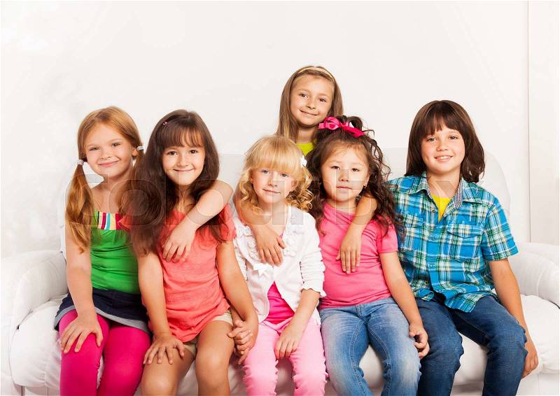 Large group of kids hugging, sitting together on the sofa at home and smiling, stock photo