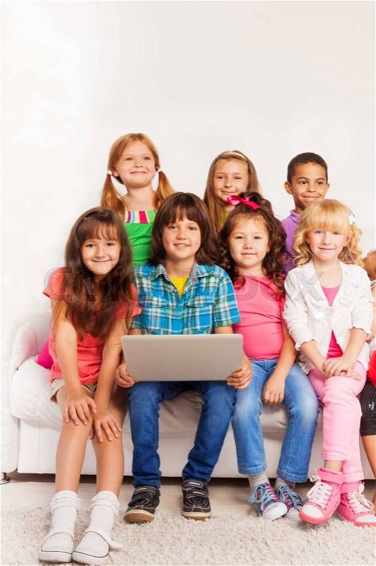 Group of happy little kids, boys and girls sitting on the coach with laptop in living room, stock photo