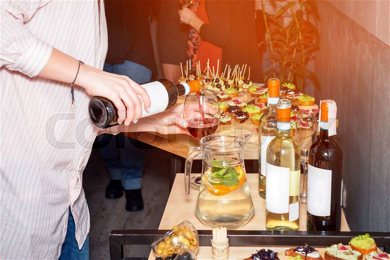 Waiter pouring red wine in a glass at a restaurant table full of appetizers with guests standing near, stock photo