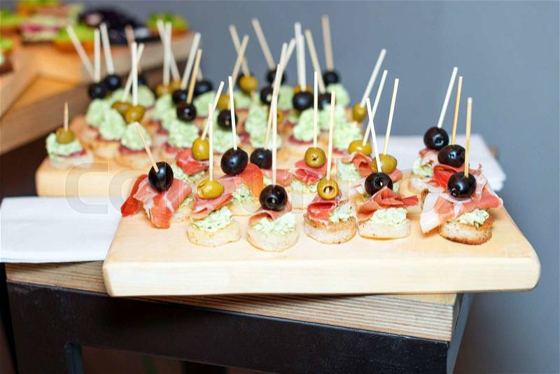 Wooden tray of appetizers on pallet coffee table at banquet with jamon, butter cream and olives, stock photo