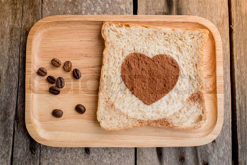 Cocoa powder forming a heart on a bread on wooden background, stock photo