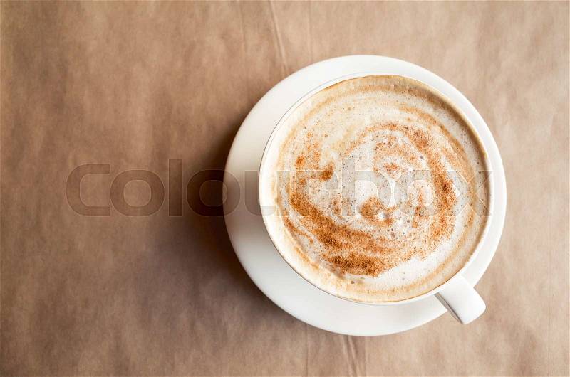 Cappuccino. Cup of coffee with milk foam stands over old paper on table in cafeteria. Top view, stock photo