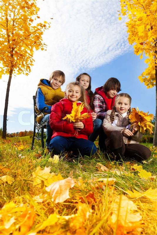 Five happy kids, boy and girls with maple leaves in the autumn park under the trees, low angle, stock photo