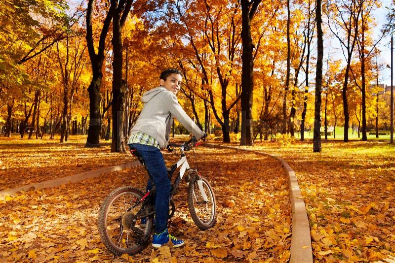 Nice black boy riding a bicycle in the autumn park full of autumn leaves turning back, stock photo