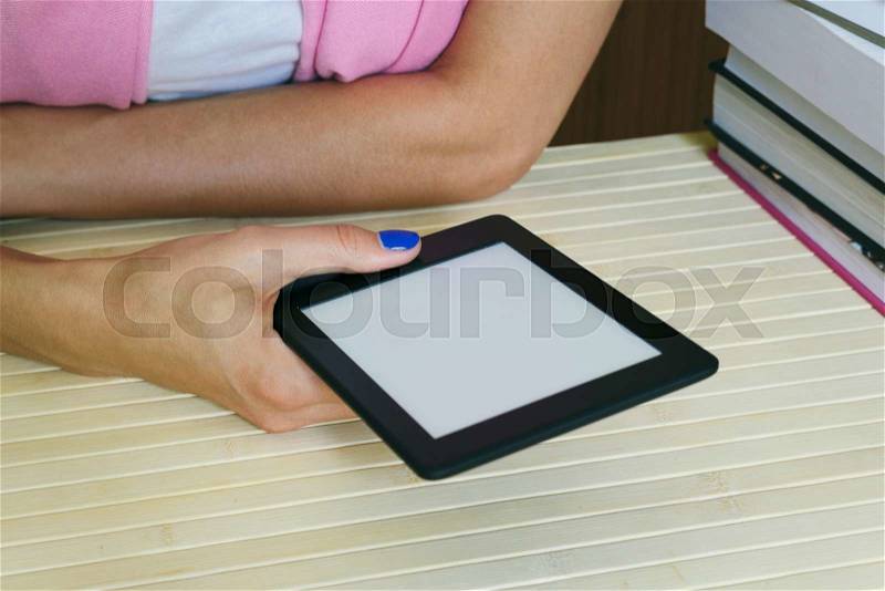 Female hands holding an e-book next to a stack of paper books, stock photo