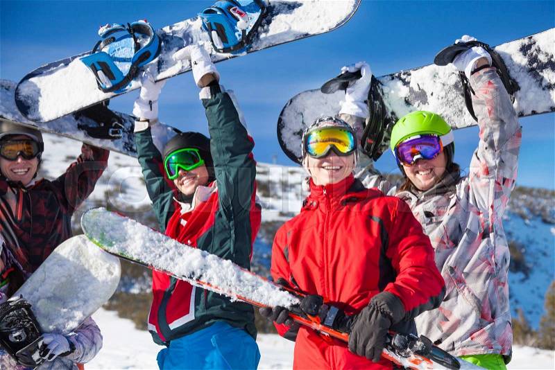Four happy friends standing together and holding snowboards and skies looking straight, stock photo