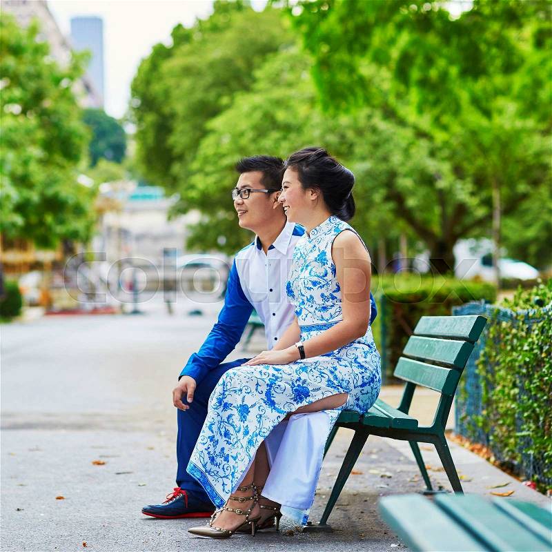 Young romantic Asian couple sitting on bench near the Eiffel Tower, Paris, France, stock photo