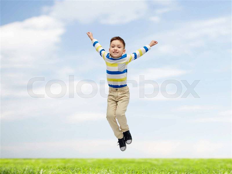 Happiness, childhood, freedom, movement and people concept - happy little boy jumping in air over blue sky and grass background, stock photo
