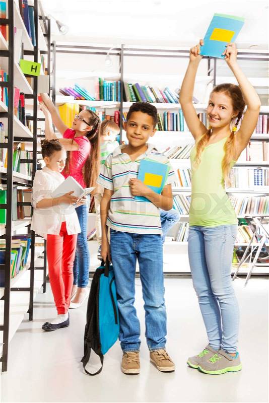 Smiling girl tries to hit boy with book in library, stock photo