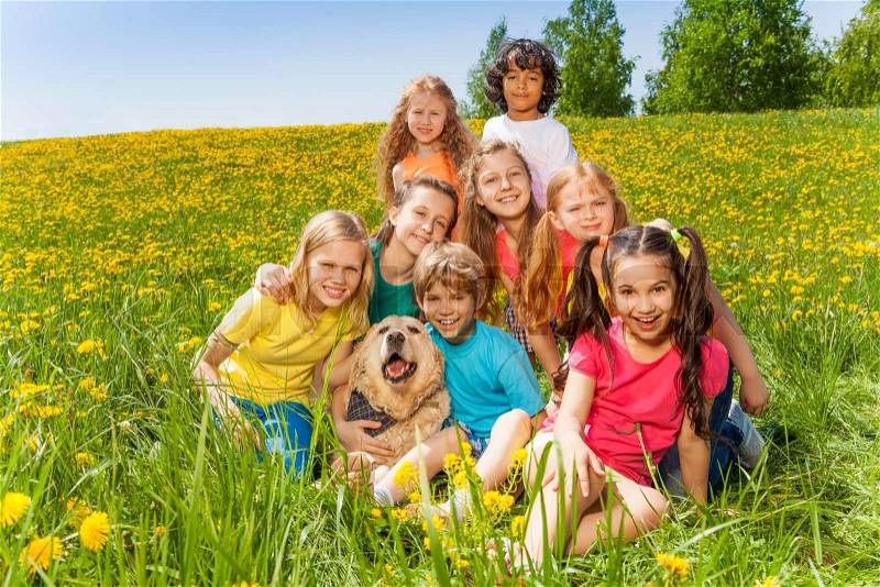 Cheerful kids with dog sitting on the green grass in summer, stock photo