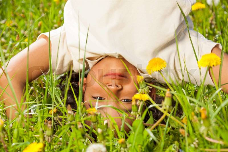 Cute curly boy standing upside down on head in dandelions field in summer, stock photo