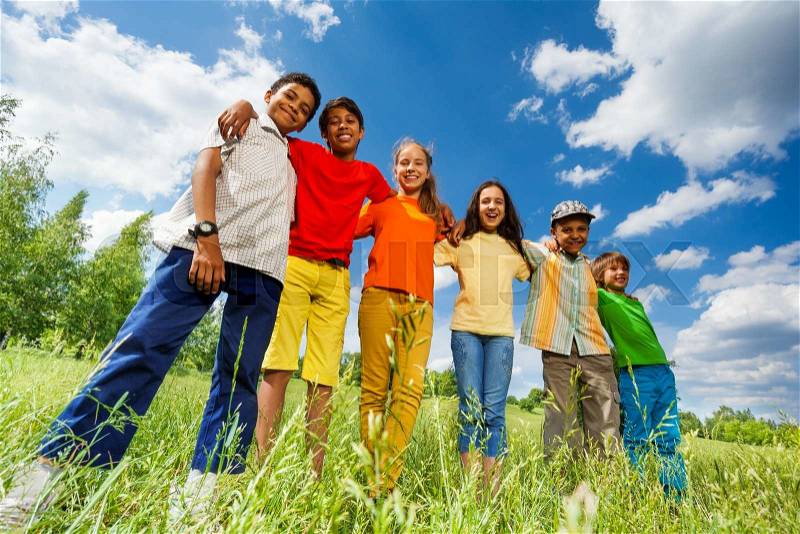 Happy kids stand in row straight and hug shoulders of each other outside, stock photo