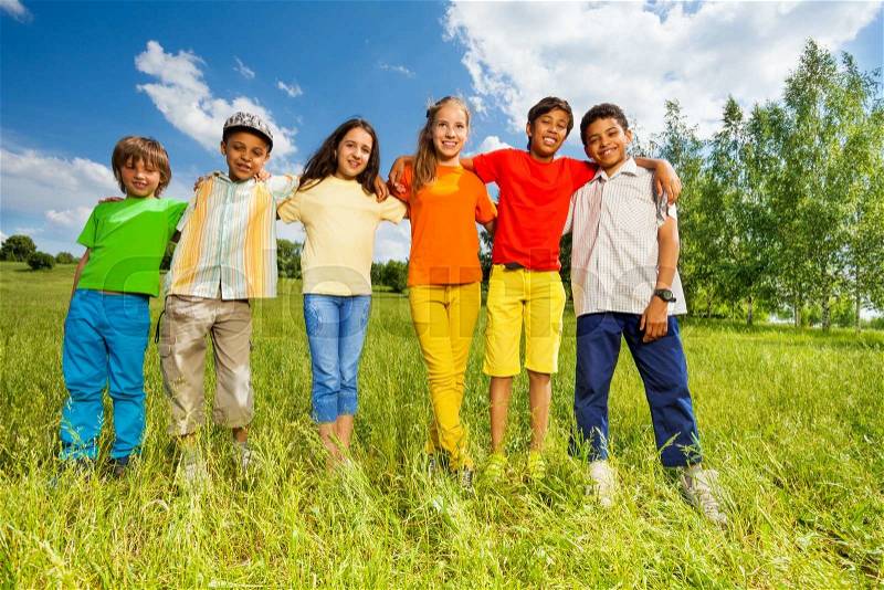 Happy kids standing in a row straight and hug shoulders of each other outside, stock photo