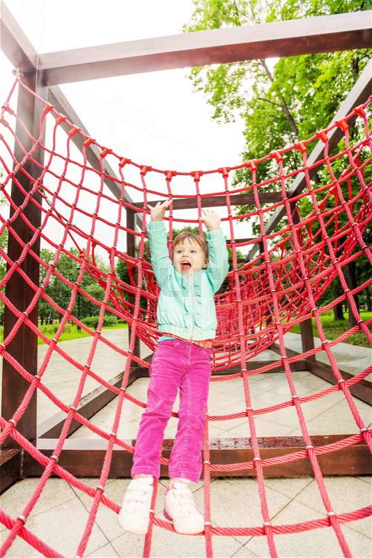 Excited girl with hands up on red net of playground construction, stock photo