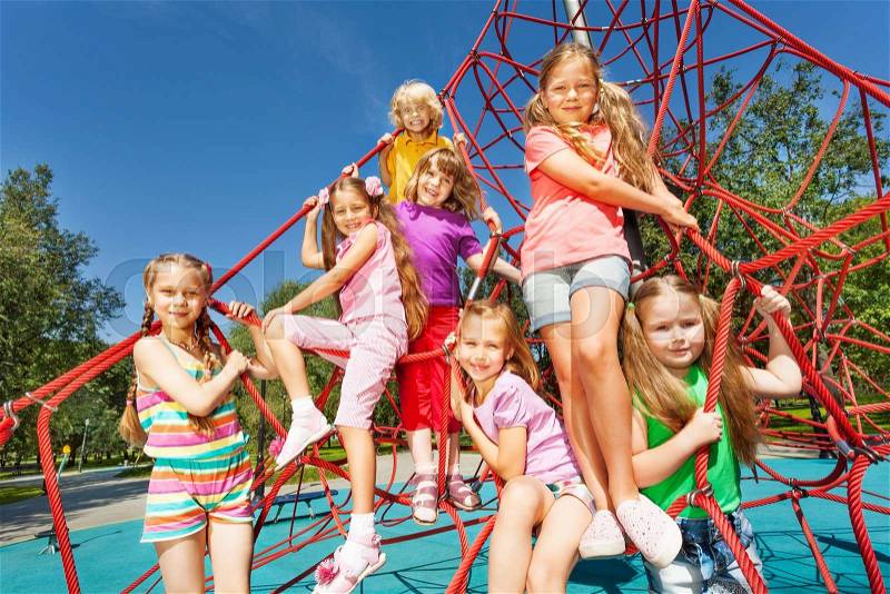 Smiling group of children sit on red ropes of playground outside in summer, stock photo