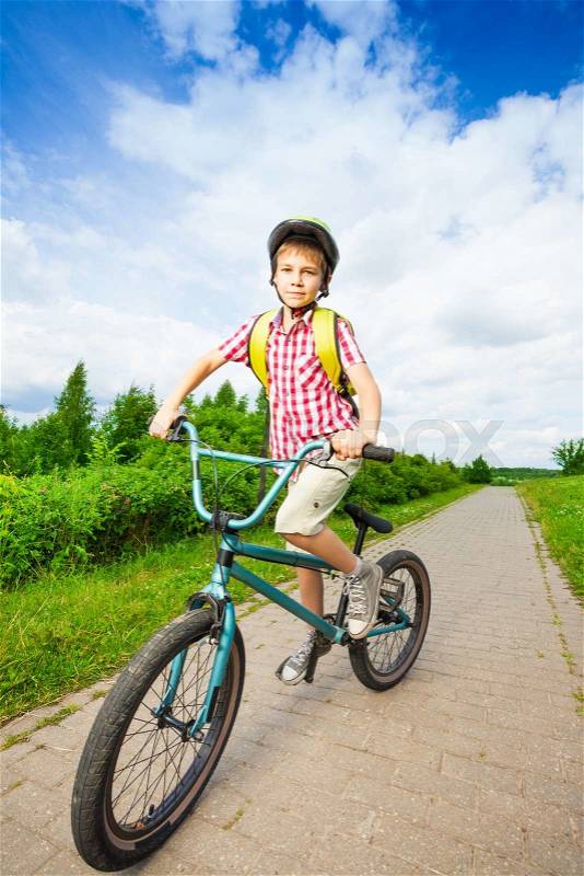 Boy in bike helmet rides his bike along the road in the park in summer, stock photo