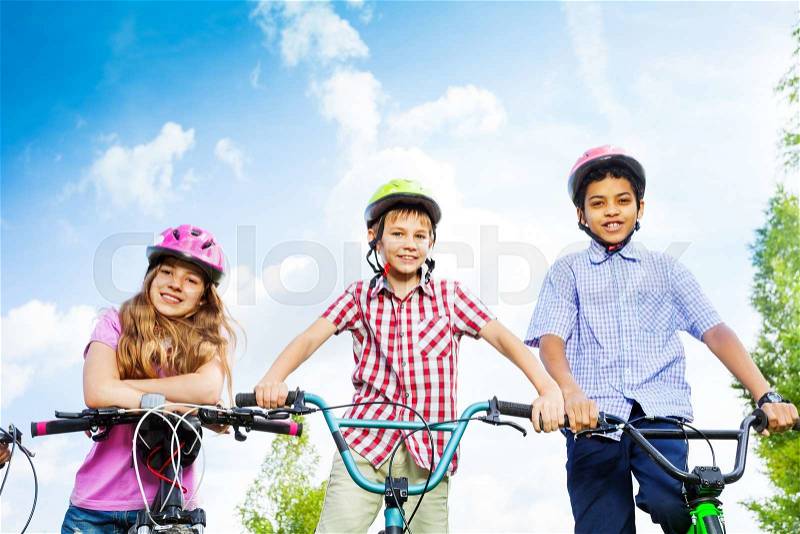 Three kids in helmets hold bike handle-bars and are ready to ride a bike, stock photo