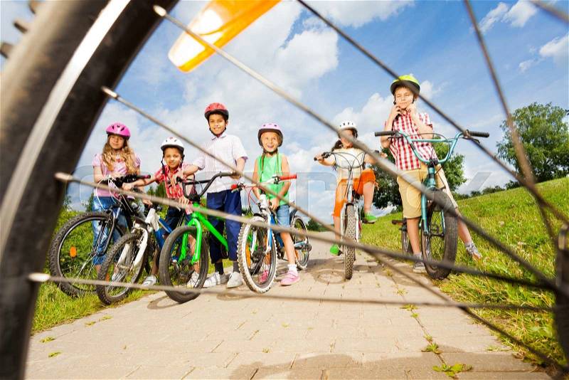 View from bicycle spoke on kids with helmets and bikes on path in field, stock photo